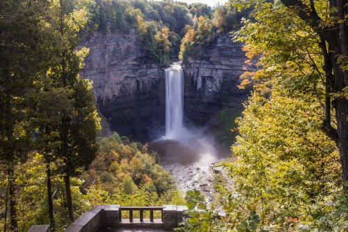 A stunning waterfall cascades into a serene pool, surrounded by vibrant autumn foliage and rocky cliffs.