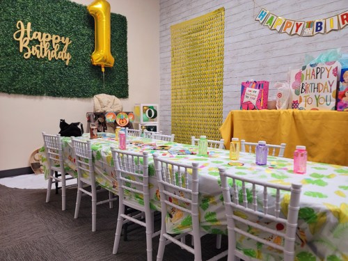 A decorated birthday party room with a long table, colorful drinks, and a "Happy Birthday" banner.