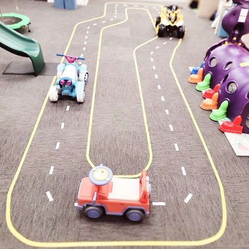 Colorful toy cars on a play mat with road markings, surrounded by a slide and a play structure.