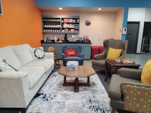 Cozy lounge area with a white sofa, blue armchair, two patterned chairs, a wooden coffee table, and colorful walls.