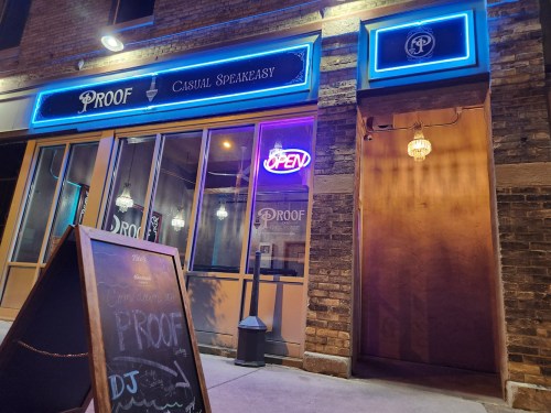 A nighttime view of a speakeasy entrance with neon lights, a chalkboard sign, and a welcoming "OPEN" sign.