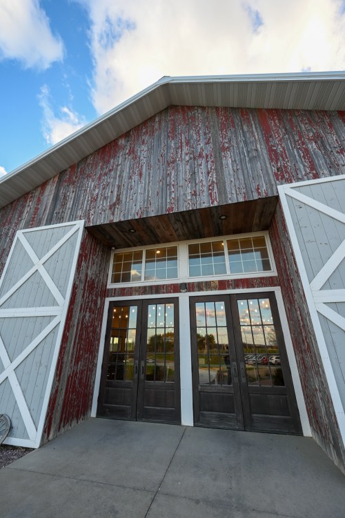 A rustic barn with a red and gray exterior, featuring large double doors and windows, set against a blue sky.