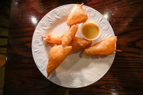 A plate of golden fried snacks with a small cup of dipping sauce on a wooden table.