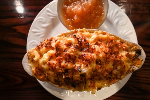 A baked macaroni and cheese dish with a golden crust, served with a side of applesauce in a small bowl.