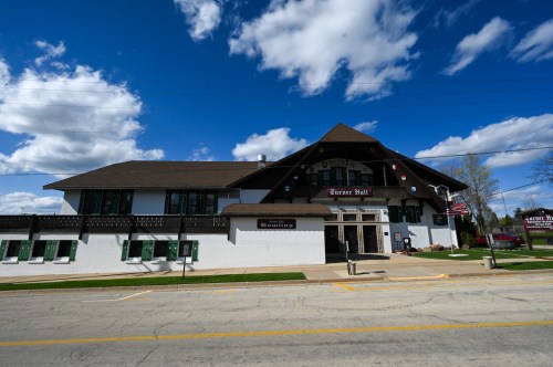 A large, two-story building with a peaked roof, featuring a sign that reads "Turner Hall" and surrounded by blue skies.