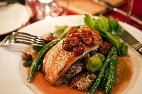 A plated dish featuring grilled fish topped with grapes, served with green beans, Brussels sprouts, and a savory sauce.