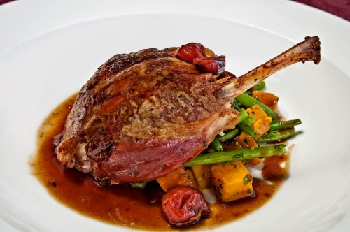 A succulent roasted duck leg served on a bed of green beans and butternut squash, drizzled with rich sauce.