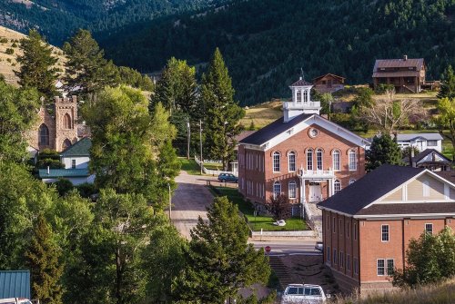A scenic view of a small town with historic buildings, trees, and mountains in the background.