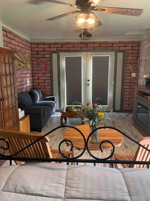 Cozy living room with a sofa, wooden furniture, and a bouquet on a table, featuring brick walls and a ceiling fan.