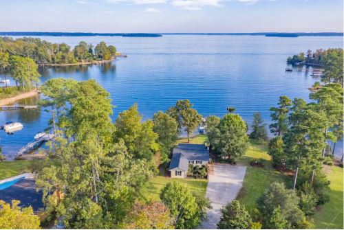 Aerial view of a serene lake surrounded by trees, featuring a house and boats on the water.