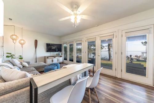 Cozy living room with a view of the lake, featuring a sofa, dining table, and large windows letting in natural light.