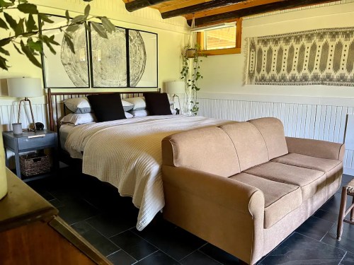 Cozy bedroom featuring a bed with white linens, a brown sofa, and decorative wall art in a bright, inviting space.