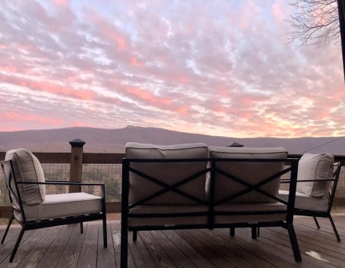 A cozy outdoor seating area with a view of a colorful sunset over mountains and clouds.