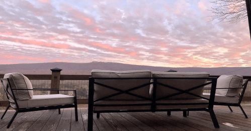 A cozy outdoor seating area with a view of a mountain at sunset, featuring pink and orange clouds in the sky.