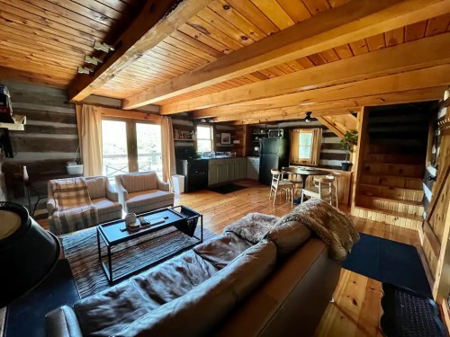 Cozy wooden cabin interior with a living area, kitchen, and dining space, featuring rustic decor and natural light.