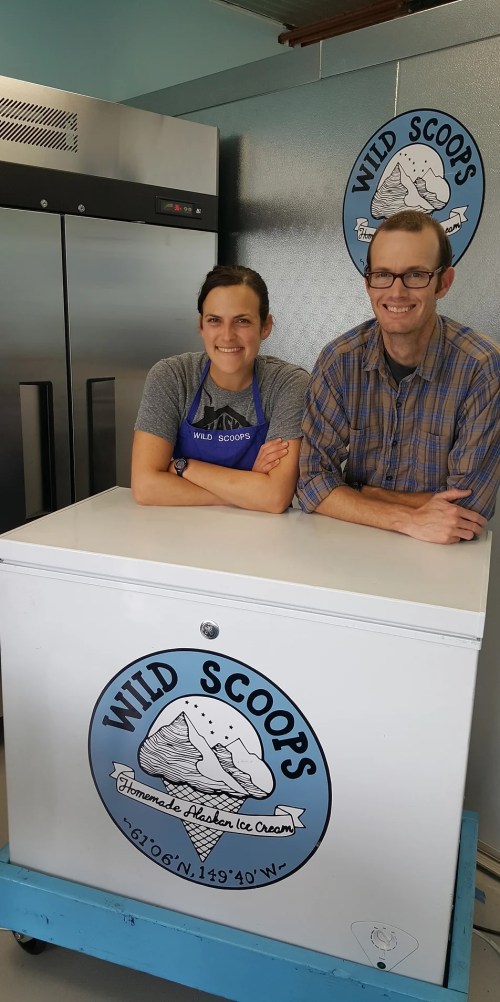 Two people stand behind a white ice cream freezer labeled "Wild Scoops," smiling in a bright, inviting space.