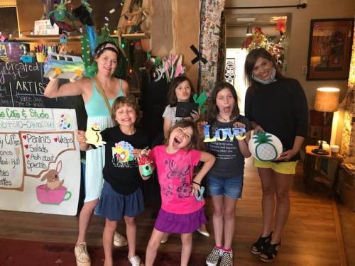 A group of five people, including children, posing playfully in an arts and crafts studio with colorful decorations.