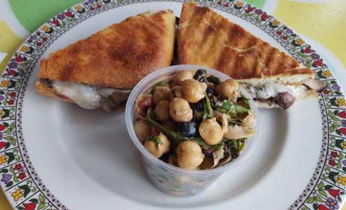 A plate with two toasted sandwiches and a small cup of mixed chickpea salad.