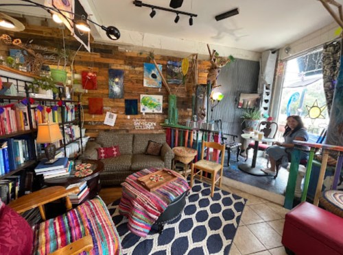 Cozy café interior with colorful decor, bookshelves, and a woman sitting at a table by the window.