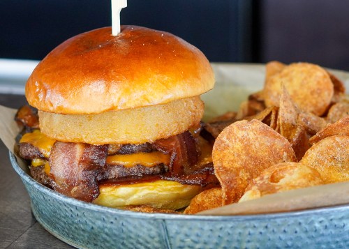 A juicy burger with bacon, cheese, and an onion ring, served with crispy potato chips on the side.