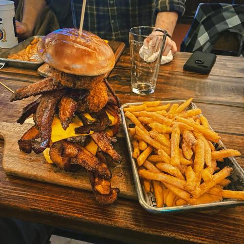 A towering burger topped with crispy bacon and cheese, served with a side of golden fries on a wooden table.