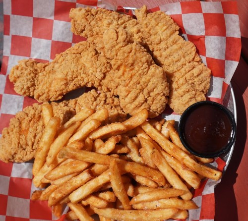 A plate of crispy fried chicken tenders with a side of golden French fries and a small cup of dipping sauce.