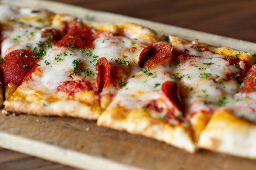 A close-up of a pepperoni pizza with melted cheese and herbs, served on a wooden board.