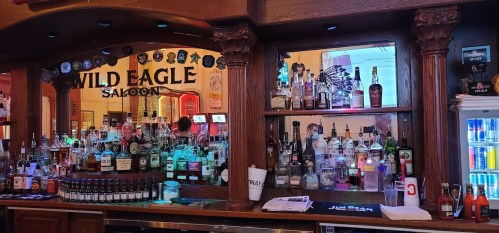 A wooden bar with various bottles of liquor, illuminated by colorful lights, at the Wild Eagle Saloon.