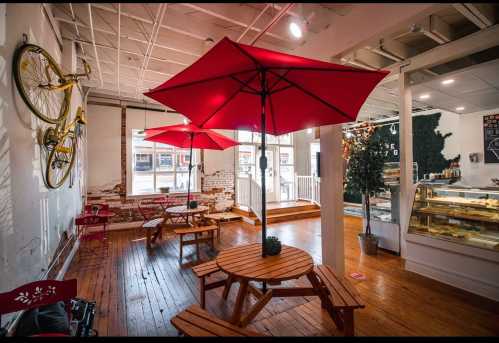 Cozy café interior with wooden tables, red umbrellas, and a display case, featuring a warm, inviting atmosphere.