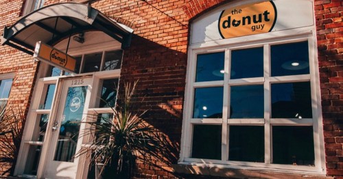 Exterior of "The Donut Guy" shop, featuring a brick facade, large windows, and a welcoming entrance.