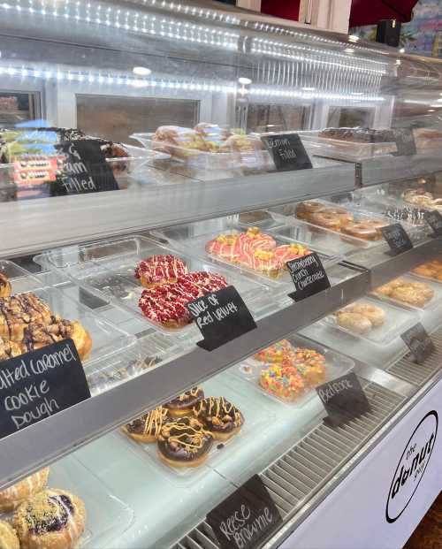 A display case filled with various colorful donuts, each labeled with their flavors.