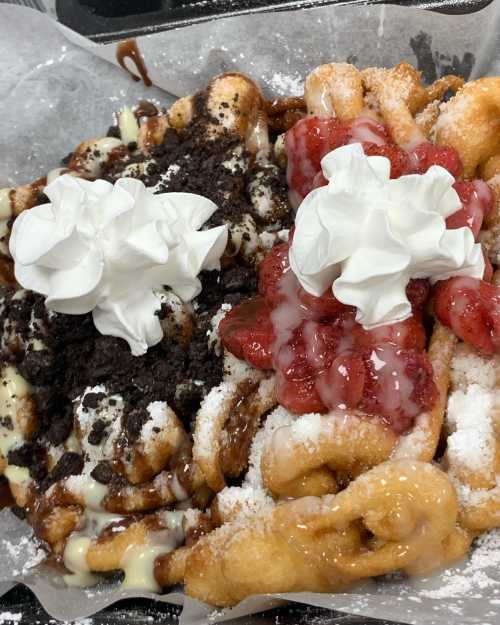 A plate of funnel cakes topped with whipped cream, chocolate, crushed cookies, and strawberry sauce.