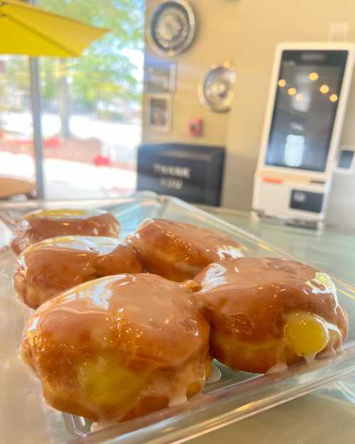 A clear plate of glazed donuts filled with yellow cream, displayed in a bright cafe setting.