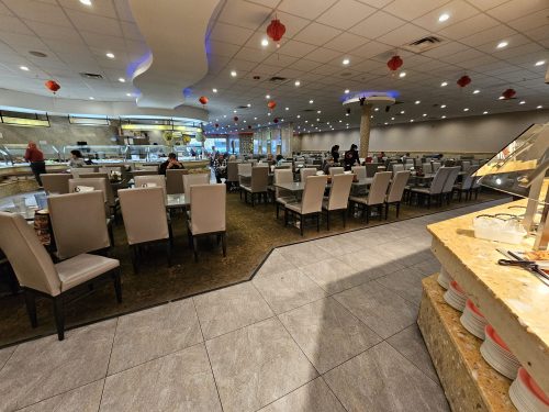 A spacious restaurant interior with numerous tables and chairs, featuring a buffet area and decorative lanterns.