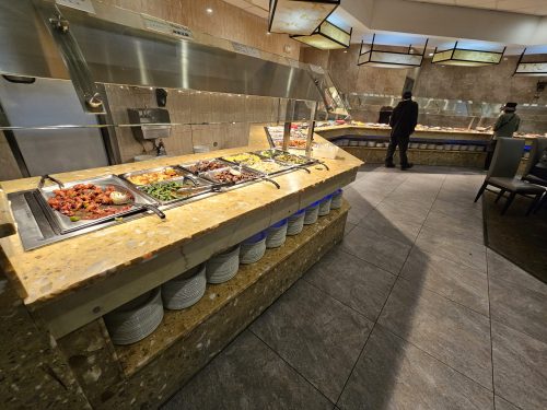 A buffet with various dishes displayed on a counter, with a person serving food in the background.