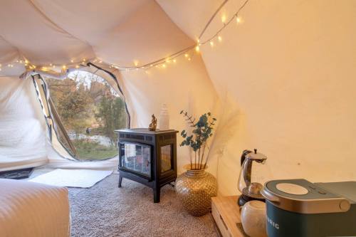 Cozy tent interior with fairy lights, a small table, a coffee maker, and decorative plants, overlooking a natural view.