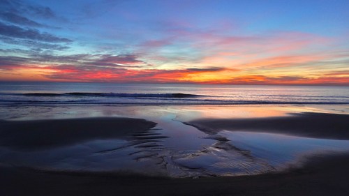 A serene beach at sunset, with vibrant colors reflecting on the water and gentle waves lapping at the shore.