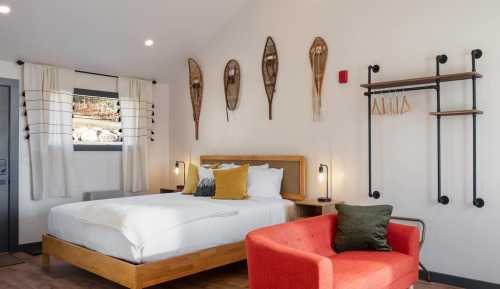 Cozy bedroom featuring a bed, red chair, and decorative snowshoes on the wall, with natural light and modern decor.