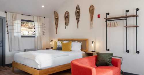 Cozy hotel room featuring a bed, red armchair, and decorative wall hangings, with natural light and modern decor.