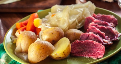 A plate of corned beef, boiled potatoes, carrots, and cabbage, served on a green dish.