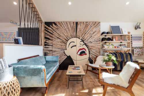 A cozy interior featuring a blue sofa, wooden chairs, a coffee table, and a striking wall art of a woman's face.