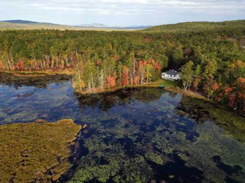 Aerial view of a serene lake surrounded by colorful autumn trees and a house nestled among the greenery.