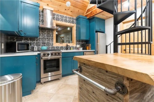 Modern kitchen with blue cabinets, stainless steel appliances, and a spiral staircase, featuring a wooden island.