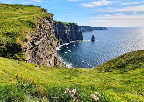 A scenic view of cliffs overlooking the ocean, with lush green grass and a rock formation in the water.