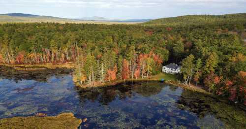 Aerial view of a serene lake surrounded by colorful autumn trees and a white house nestled in the forest.