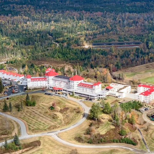Aerial view of a large hotel surrounded by colorful autumn trees and winding roads.