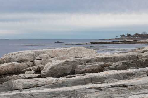 Rocky shoreline with calm waters and a cloudy sky in the background.