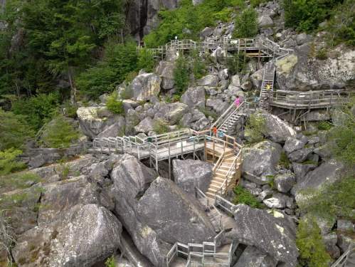 Wooden walkways and platforms weave through large boulders and greenery in a rocky outdoor landscape.