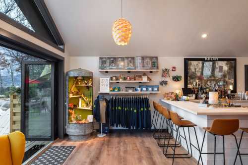 A cozy bar area with a modern design, featuring a counter, shelves of items, and a bright pendant light.