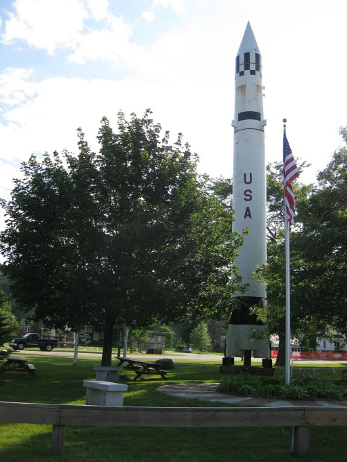 A tall rocket monument labeled "USA" stands in a park, surrounded by trees and an American flag.